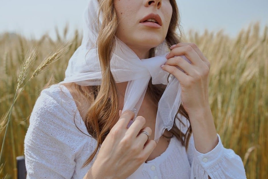 Crop woman in white headscarf sitting on grassy field